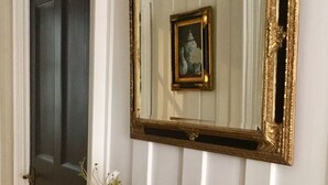 A white door with a dark door frame, a gold-framed mirror above a mantel with pinecones and small potted plants, and a white railing below. - Fabulous Apt Historic House St Aubin (St. Brelade)