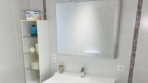 A bathroom with a white sink, dark cabinetry, a mirror, and a shelf with toiletries. - Villa with terrace 200m from the beach (Six-Fours-les-Plages)