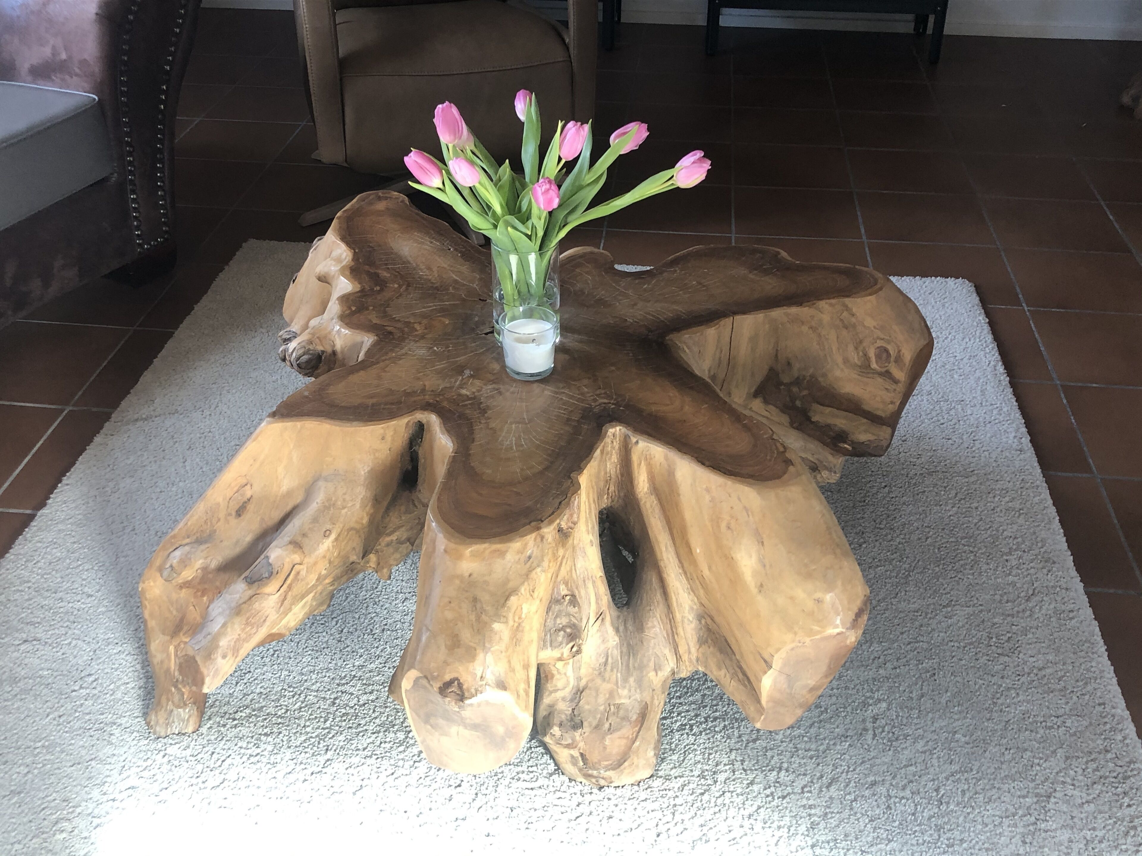 A wooden coffee table with a unique design, featuring a vase with pink flowers and a candle.