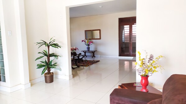 A spacious living room with a large potted plant, a wooden coffee table, and a red vase with flowers. - Serpa Hotel (Itacoatiara)