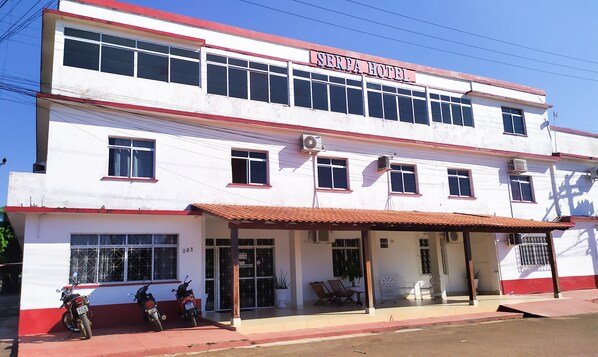A two-story building with a sign reading "SERPA HOTEL". There are two motorcycles parked in front, and a covered area with chairs and a potted plant. - Serpa Hotel (Itacoatiara)