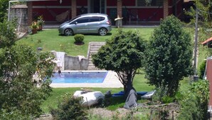 Una casa con techo de tejas rojas, piscina y un coche estacionado al frente.