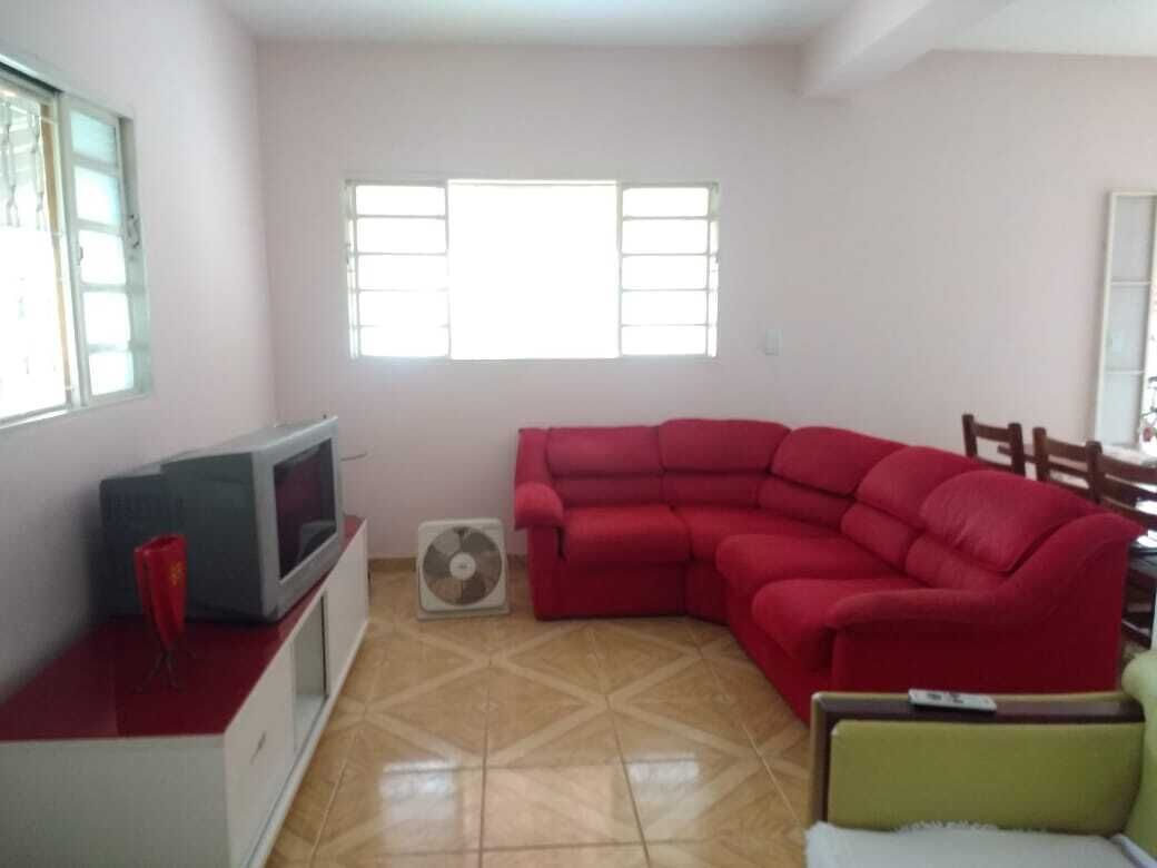 Un soggiorno con un divano rosso, una TV su un mobile, una ventola e una finestra con persiane.