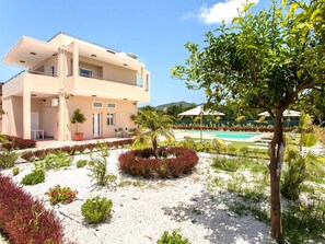 Ein zweistöckiges Gebäude mit Pool, umgeben von angelegten Gärten und blauem Himmel.