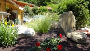 Un jardin où l’on trouve une grande variété de plantes et de fleurs, un gros rocher et, au loin, une montagne.