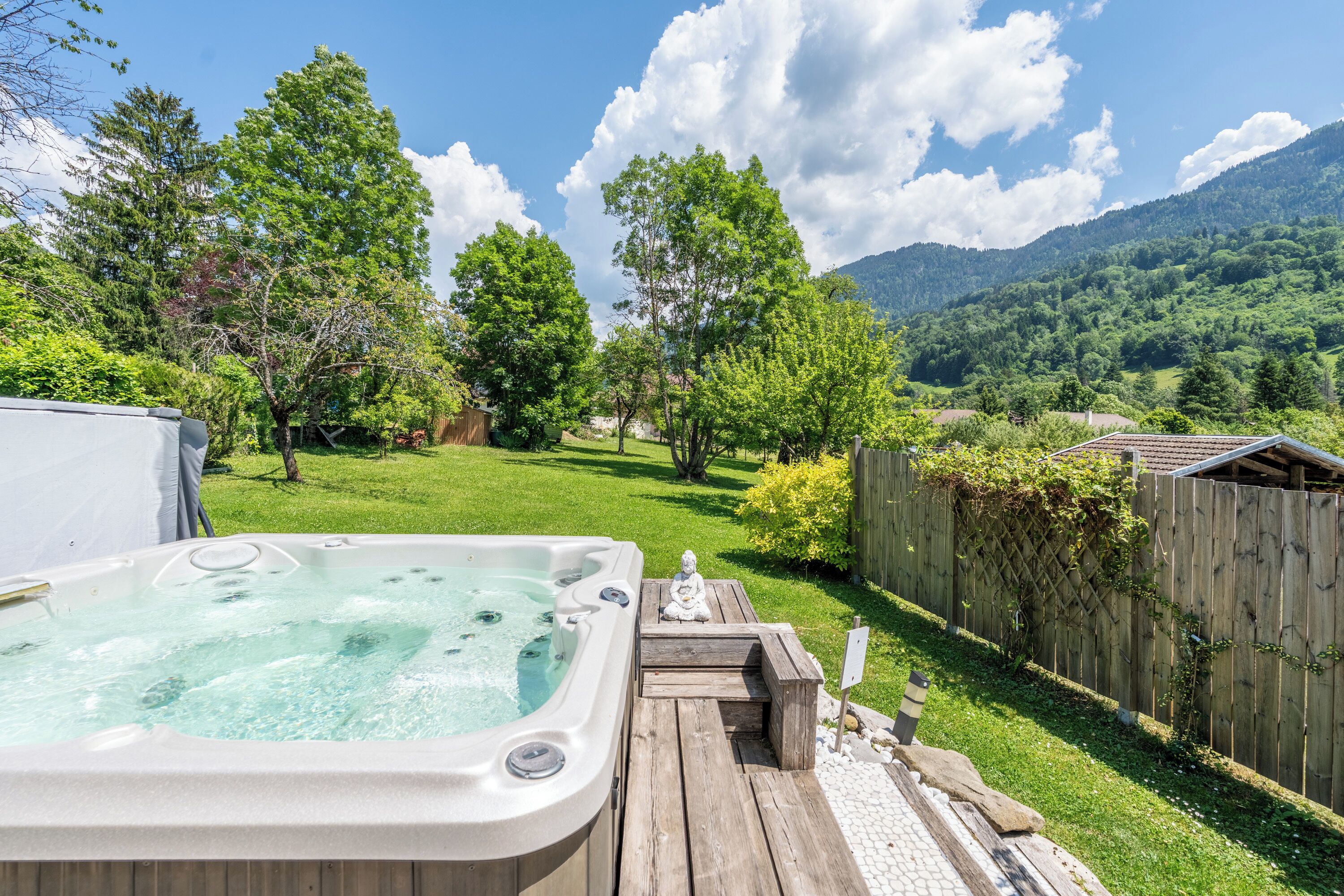 Un bain à remous sur une terrasse en bois, avec vue sur un paysage verdoyant et luxuriant ainsi que sur des montagnes.