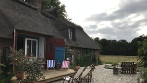 Une maison de campagne au toit de chaume, avec une terrasse en bois et deux chaises de plage.