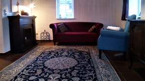 Un salon avec une cheminée, un canapé rouge, un fauteuil bleu et un tapis à motifs.