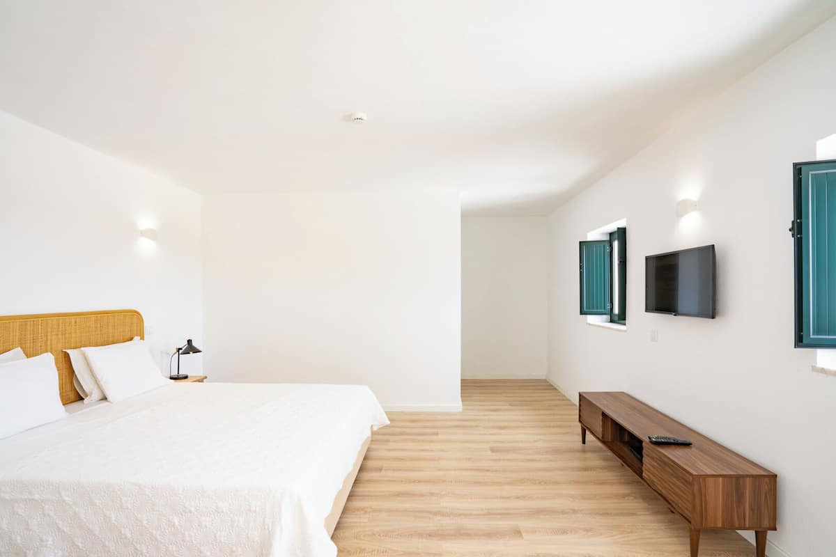 A modern hotel room with a large bed, a wooden bench, a TV mounted on the wall, and a small table.