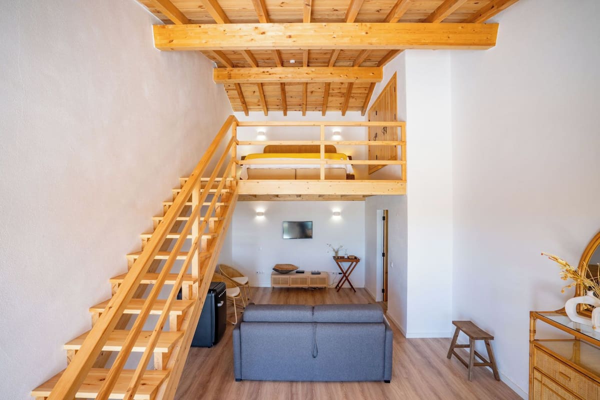 A multi-level wooden interior with a staircase, a sofa, a small table, and a television.