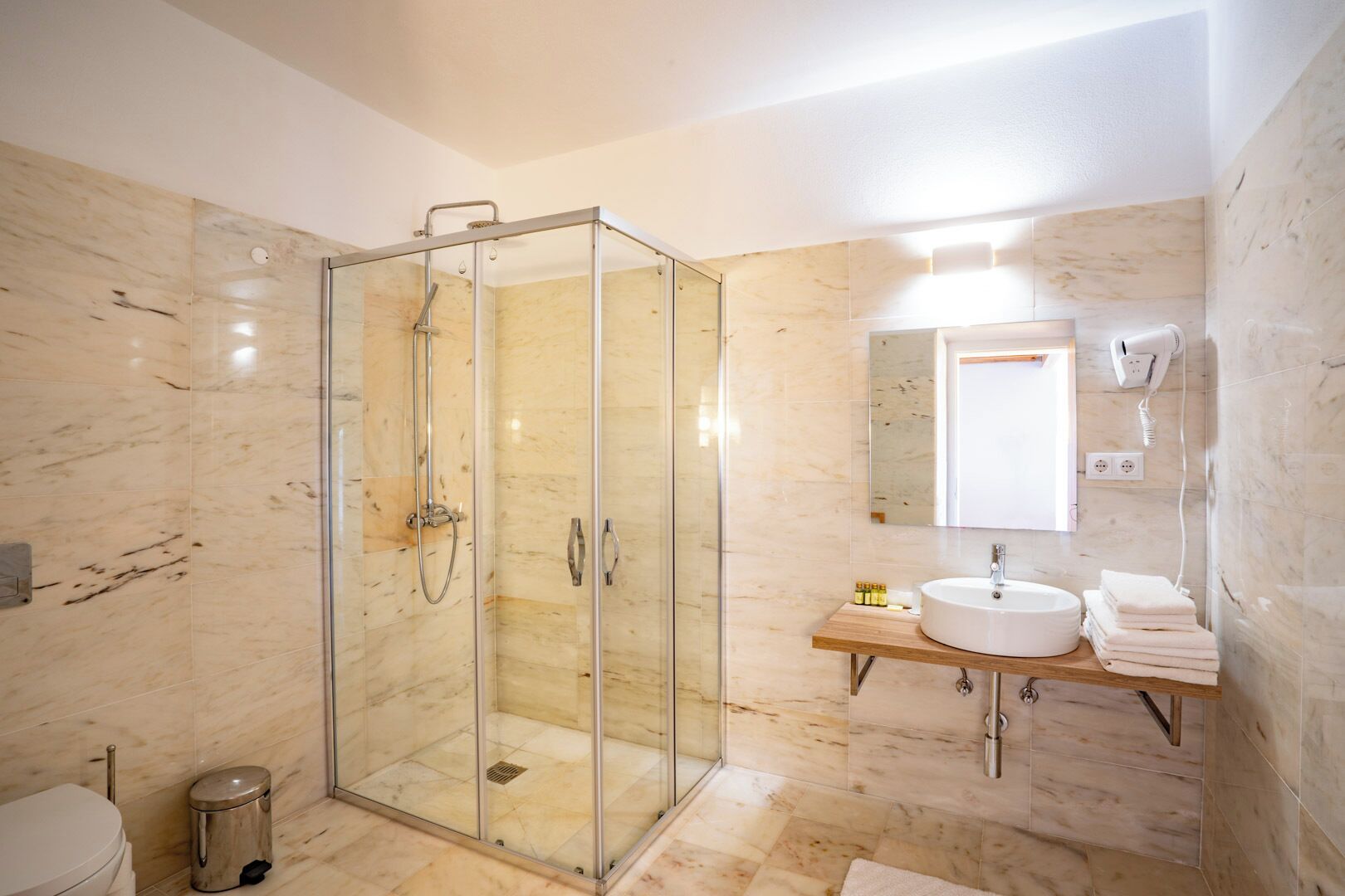 A modern bathroom with a glass-enclosed shower, a marble-tiled floor, a sink with a mirror, and a toilet.