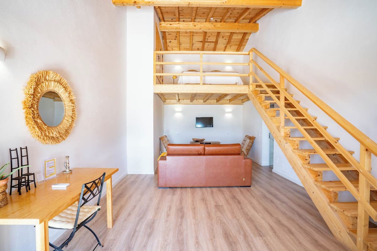 A loft-style room with a wooden staircase, a sofa, a dining table, and a TV.