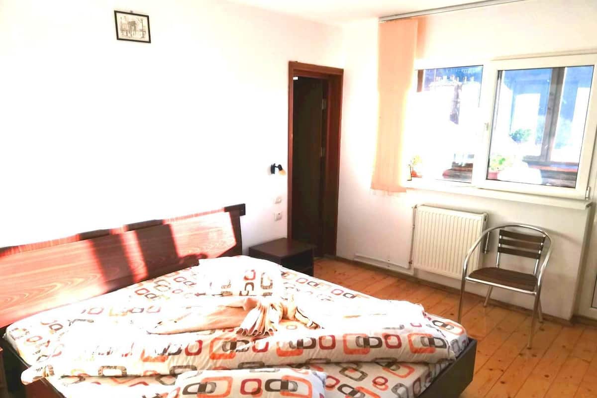 A bedroom with a bed, a chair, a radiator, and a window with a view.