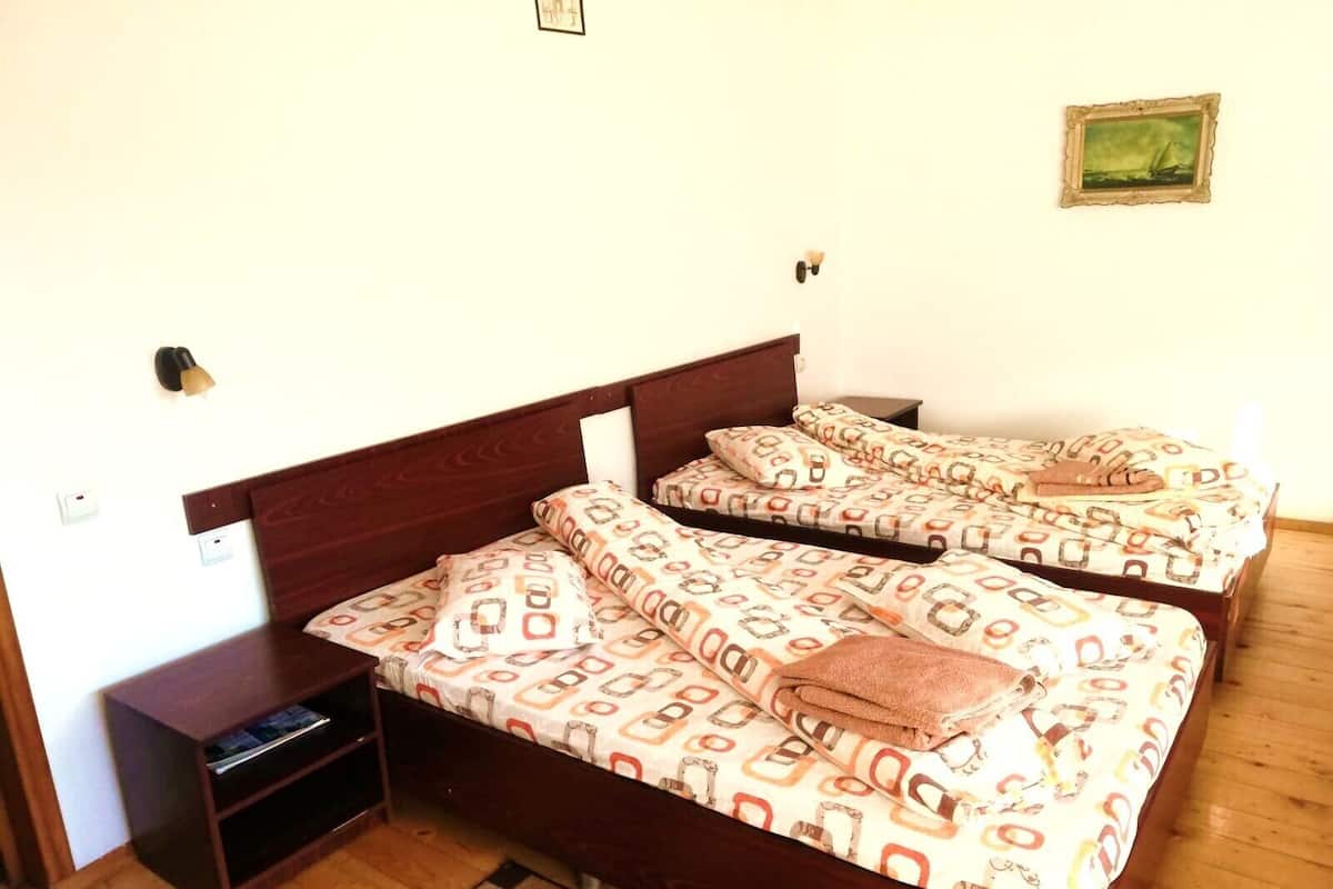 A room with two single beds, wooden headboards, a small bedside table, a wall-mounted lamp, and a framed picture.