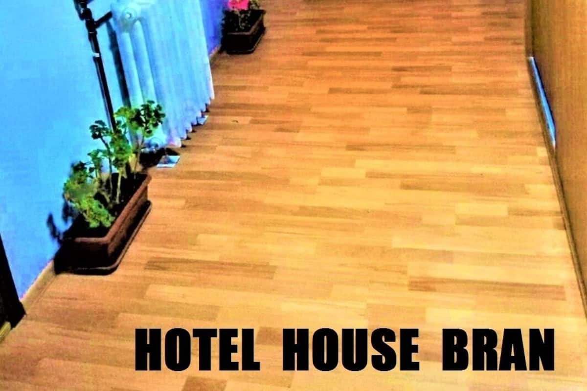 A hotel hallway with wooden flooring, a radiator, potted plants, and a door with a 'no smoking' sign.