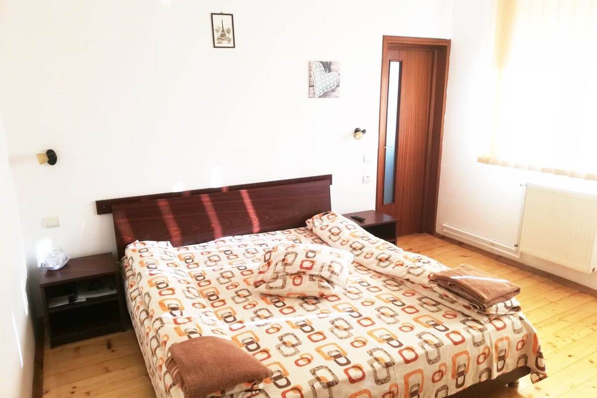 A bedroom with a wooden bed, a bedside table, a nightstand, a door, and a window with curtains.