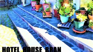 A hotel house with a covered outdoor area, steps leading up to a windowed porch, and various potted plants. - Hotel House Bran (Busteni)