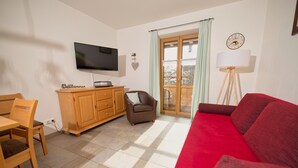 Ein Wohnzimmer mit einem roten Sofa, einem Holzkabinett, einem Fernseher und einem Essbereich mit Tisch und Stühlen.