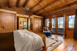 A log cabin interior with a bed, wooden walls, a large window, and a view of the outdoors.