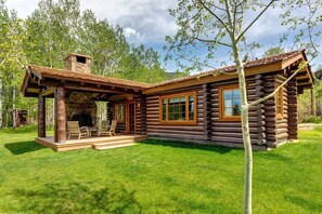 A log cabin with a fireplace, outdoor seating, and a grassy yard.