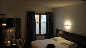 Habitación de hotel con una cama, un escritorio con lámpara, una silla, un televisor y una ventana con cortinas.