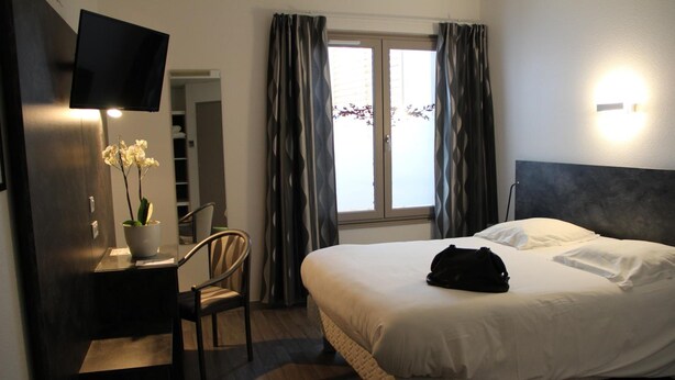 A hotel room with a bed, a desk, a chair, a TV, and a window with curtains. - Hotel Restaurant Le Tout Va Bien (Valence)
