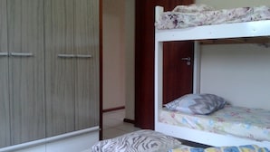 A bunk bed with a floral bedspread and two pillows, a wooden wardrobe with sliding doors, and a tiled floor. - Casa de Temporada Praia Santinho Inglese (Florianópolis)