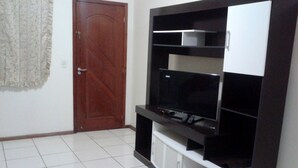 A living room with a TV on a stand, a door, and a tiled floor. - Casa de Temporada Praia Santinho Inglese (Florianópolis)