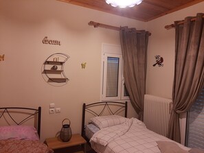 A bedroom with two beds, a window with curtains, a wall-mounted shelf, and a radiator.
