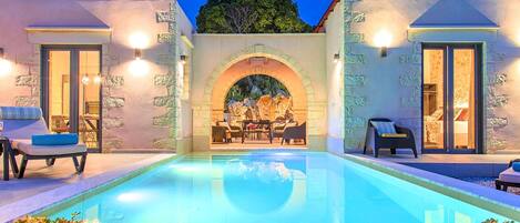 Una piscina con un arco de piedra, sillas de descanso y una zona de comedor con mesa y sillas.