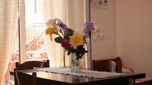 A dining table with a floral vase, chairs, and a view of a building through a window. - Studio Apartment on the Beach (Becici)