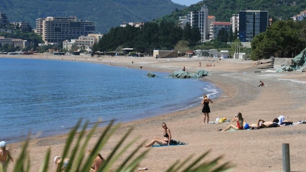 A beach with people sunbathing and swimming, buildings in the background, and a clear sky. - Studio Apartment on the Beach (Becici)