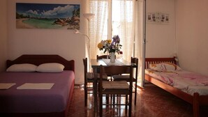 A bedroom with a bed, a small table with chairs, and a painting of a beach scene. - Studio Apartment on the Beach (Becici)