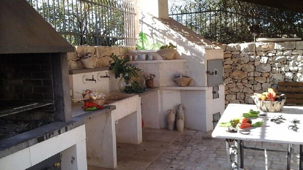 An outdoor kitchen area with a stone wall, a grill, and a table with vegetables.