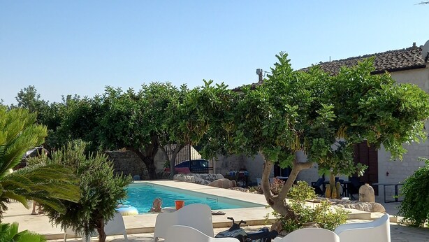 Un espace piscine avec des chaises longues blanches, une terrasse en pierre et un ciel d’un bleu éclatant.