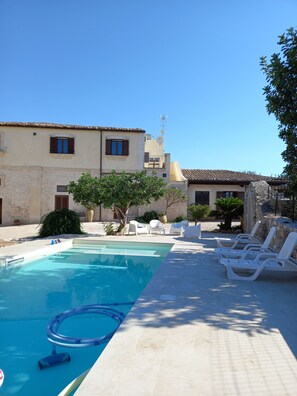A swimming pool with lounge chairs, a stone wall, and a building with a tiled roof.