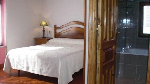 A bedroom with a wooden bed frame, a bedside table with a lamp, and a tiled floor. - Casa Pancho (Llanes)