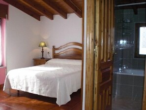 A bedroom with a wooden bed frame, a bedside table with a lamp, and a tiled floor. - Casa Pancho (Llanes)