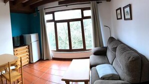 A room with a sofa, a table, a TV, and a window with curtains. - Casa Pancho (Llanes)