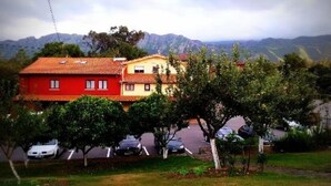 A two-story building with a red and yellow facade, surrounded by trees and parked cars. - Casa Pancho (Llanes)