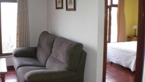 A room with a grey sofa, two framed pictures on the wall, a bed with white bedding, and a window with curtains. - Casa Pancho (Llanes)