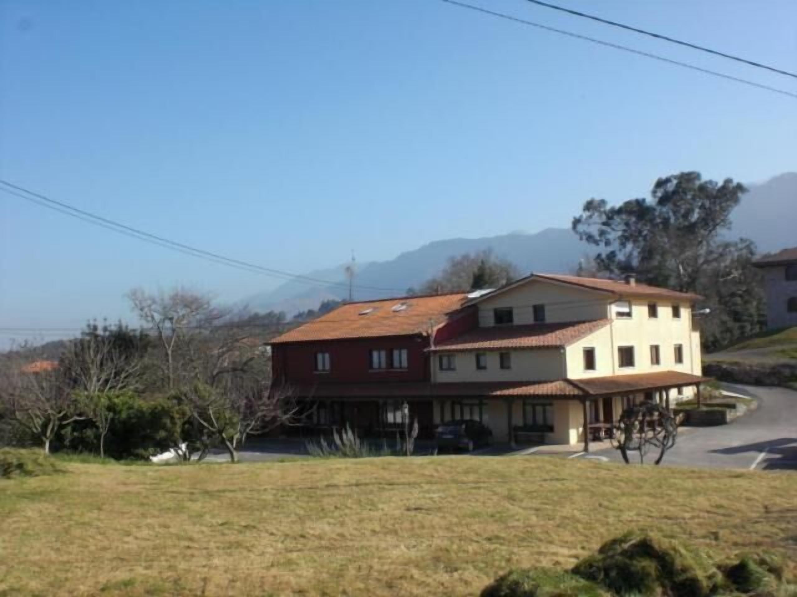 A two-story house with a red roof and a beige facade, located on a hillside with a clear view of the surrounding landscape.