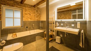 A modern bathroom with a large bathtub, a separate shower area, and a vanity with a mirror. - KajüteSiebenZwo - Holidays in a thatched house (St.Peter-Ording)