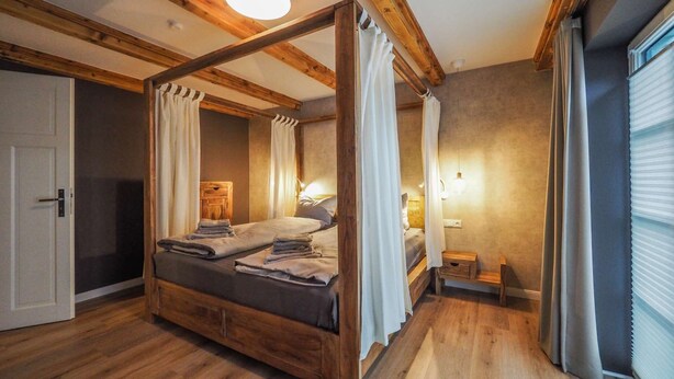 A four-poster bed with a wooden frame, a bedside table, and a nightstand. - KajüteSiebenZwo - Holidays in a thatched house (St.Peter-Ording)