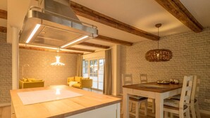A kitchen with a wooden island, a dining table with chairs, and a hanging light fixture. - KajüteSiebenZwo - Holidays in a thatched house (St.Peter-Ording)