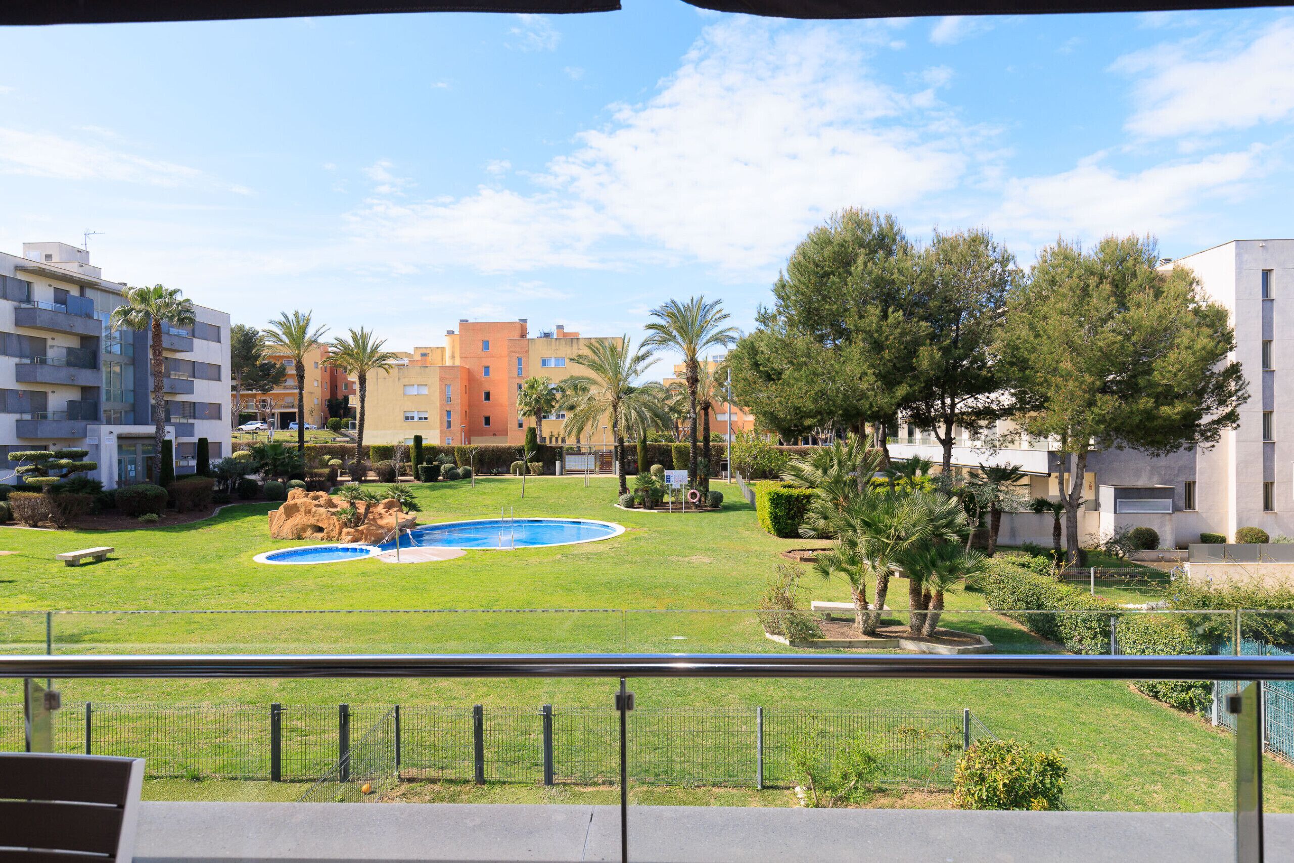 A courtyard with a swimming pool, palm trees, and apartment buildings in the background.