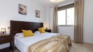 A neatly made bed with a wooden headboard, two bedside lamps, and a window with curtains. - High Standard Apartment with Pool - UHC SALOU VILLA FAMILY COMPLEX 241 (Salou)