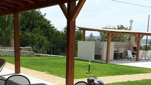 Een buitenterrein met terras, met een overdekte zithoek, inclusief een tafel en stoelen.