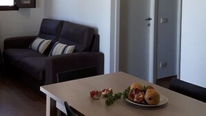 Een moderne woonkamer met een bank, een eettafel met een bord eten en een grote plafondlamp.