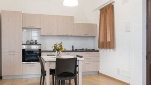 Een moderne keuken met lichte houten kastjes, een centraal eiland en een eethoek met een tafel en stoelen.